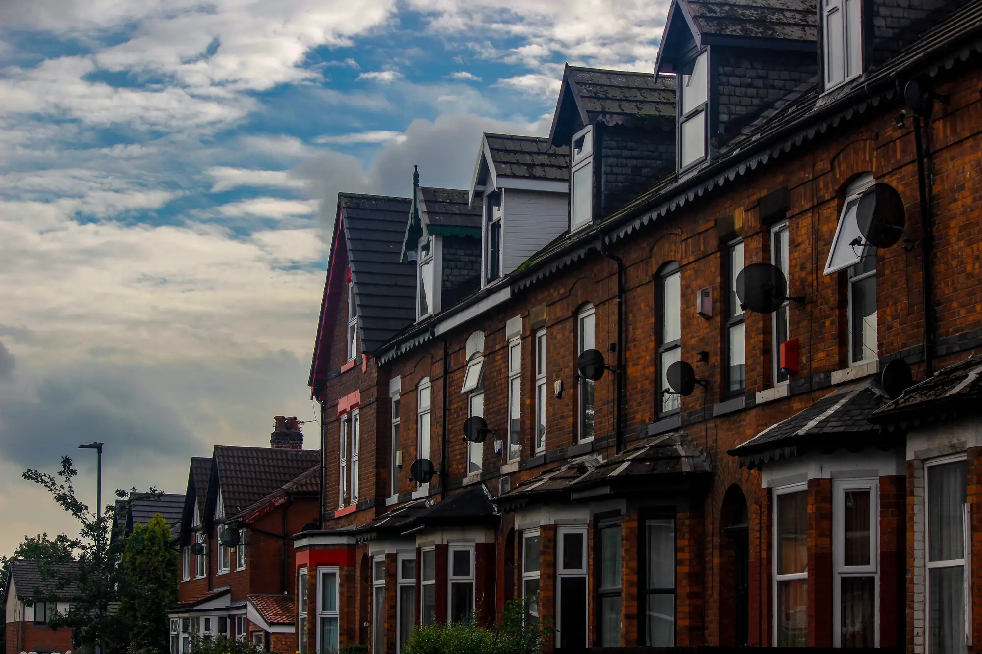 A row of red-brick terraced houses with slate roofs and dormer windows under an evening sky